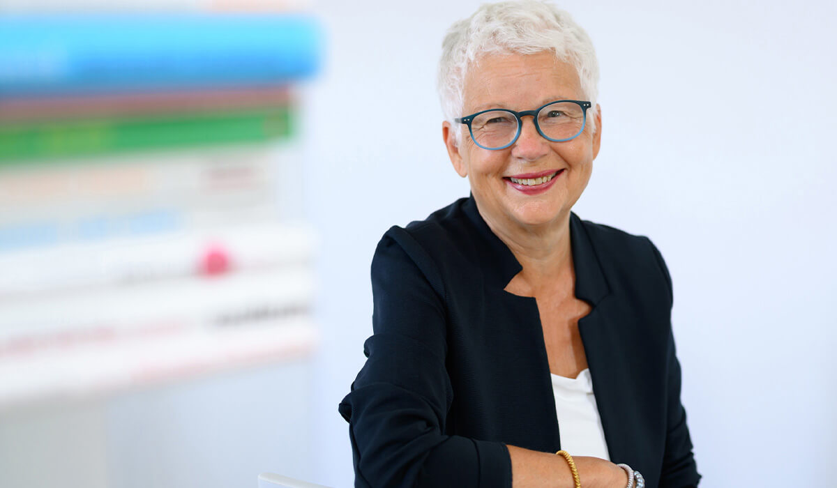 Gundula Bunge-Glenz, Zahntechnikermeisterin und zertifizierter Coach bei aussichtsreich, im dunklen Blazer neben einem Bücherstapel